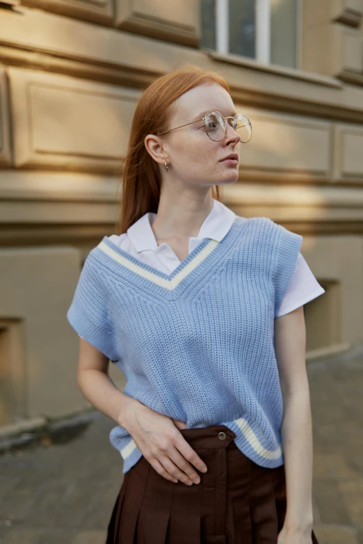 a woman standing on a sidewalk in front of a building, wearing a light blue shirt, preppy style, wearing v - neck top, met collection