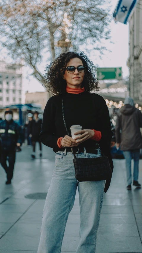 a woman standing on a sidewalk holding a cup of coffee, trending on pexels, happening, black turtleneck, curly haired, cinematic outfit photo, 🤠 using a 🖥