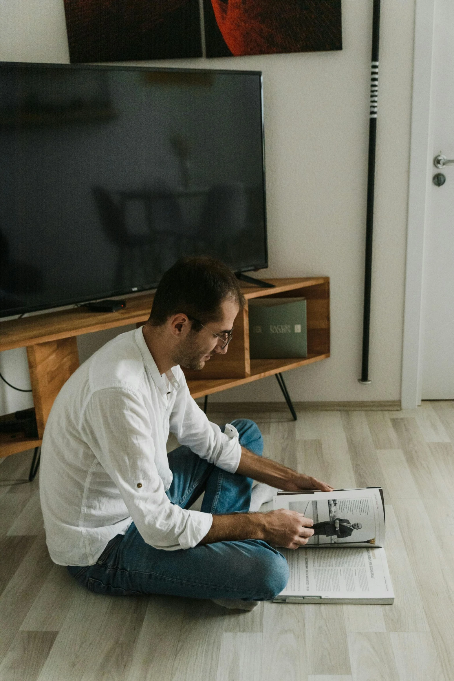 a man sitting on the floor reading a book, a cartoon, by Adam Marczyński, pexels contest winner, tv still, apartment, low quality photo, profile picture