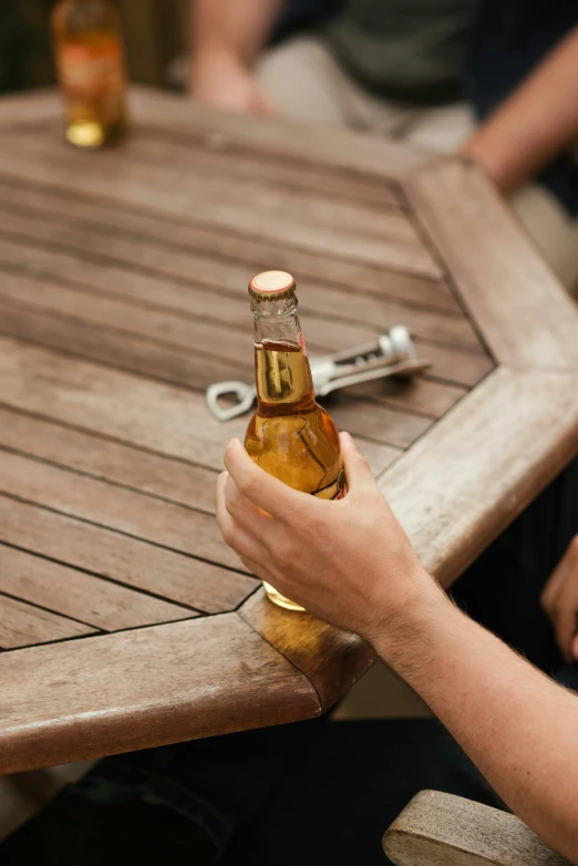 a person sitting at a table with a bottle of beer, pexels contest winner, light tan, gold, broken down, al fresco