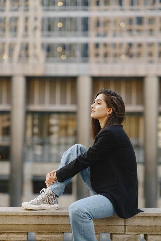 a woman sitting on a ledge in front of a building, maya ali, looking to the sky, warmly lit, in a square