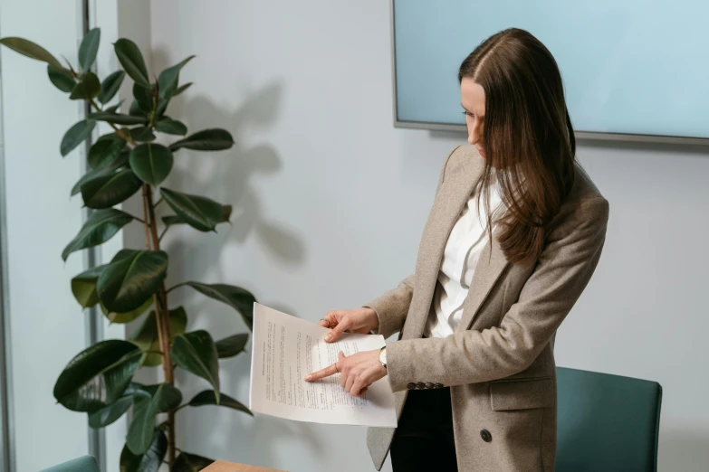 a woman standing in a room holding a piece of paper, by Carey Morris, pexels contest winner, sat in an office, bending down slightly, realistic information, slightly minimal