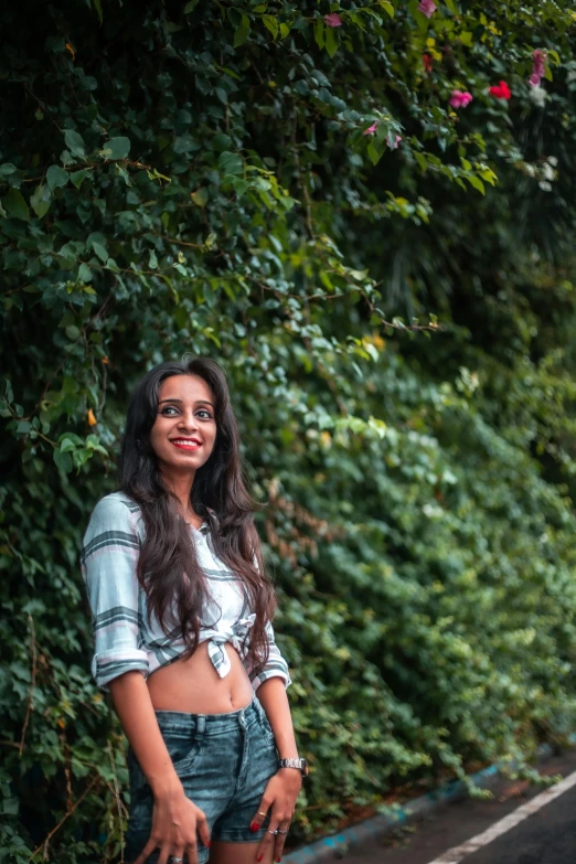 a woman standing on the side of a road, by Max Dauthendey, pexels contest winner, smiling young woman, wearing a cropped top, dense with greenery, at a park