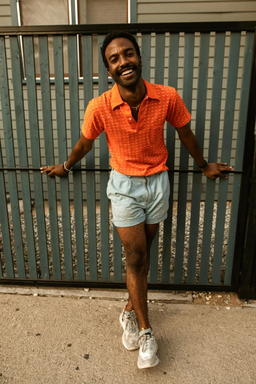 a man is standing in front of a gate, by Nathalie Rattner, pexels contest winner, wearing red shorts, dark skin tone, long and orange mustache, dressed in 1970s menswear