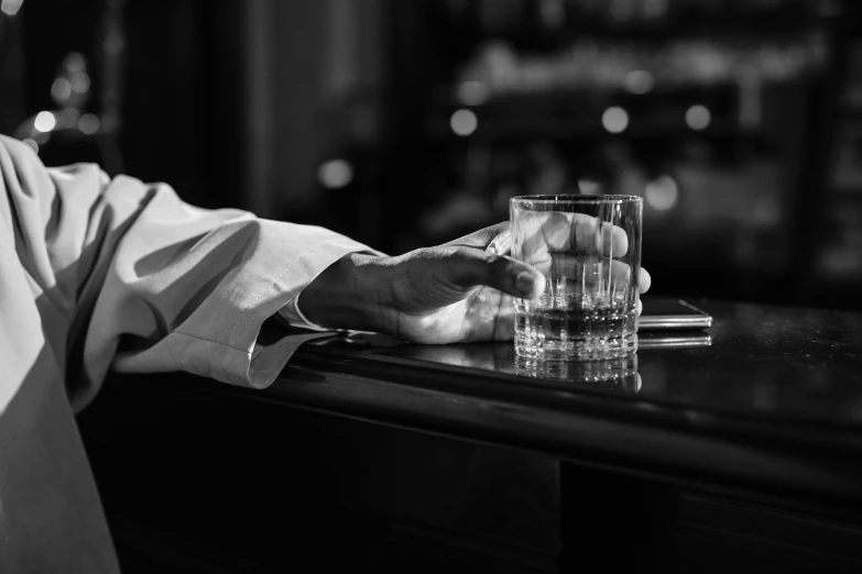 a man sitting at a bar holding a glass, a black and white photo, by Mathias Kollros, pexels, full of glass. cgsociety, hand on table, by joseph binder, gentleman