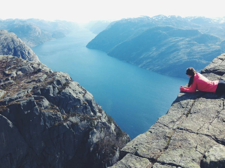 a woman sitting on top of a cliff next to a body of water, by Jesper Knudsen, pexels contest winner, high elevation, peak experience ”, high angle, youtube thumbnail