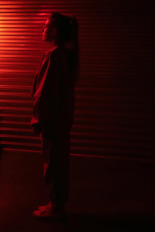 a person standing in front of a red light, showstudio, lurking in the shadows, bella poarch, low light cinematic