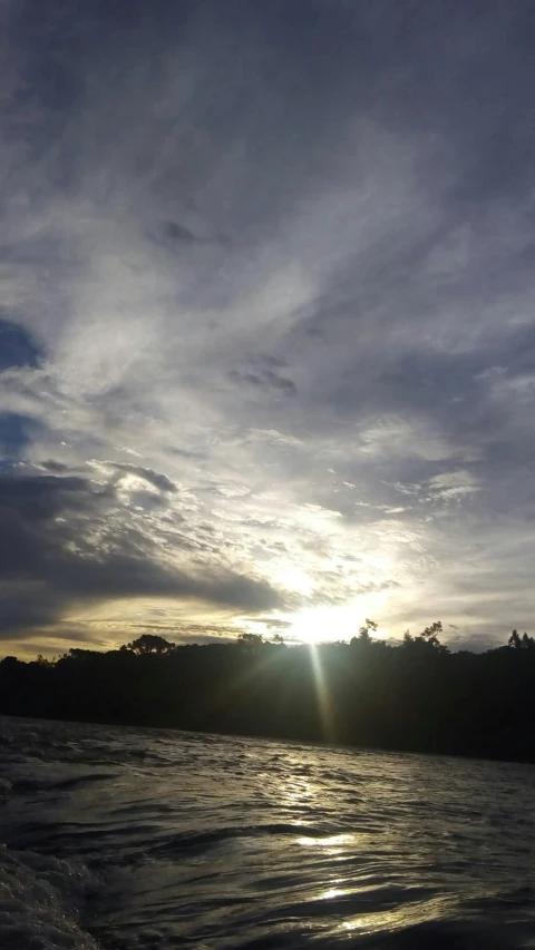 the sun is setting over a body of water, a picture, by Yosa Buson, sumatraism, gray sky with wispy clouds, near a river, low quality photo, instagram post