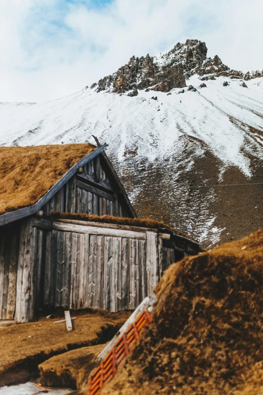 a small building with a grass roof in front of a mountain, inspired by Þórarinn B. Þorláksson, trending on unsplash, renaissance, 1940s photo, winter setting, superb detail 8 k, 1970s photo