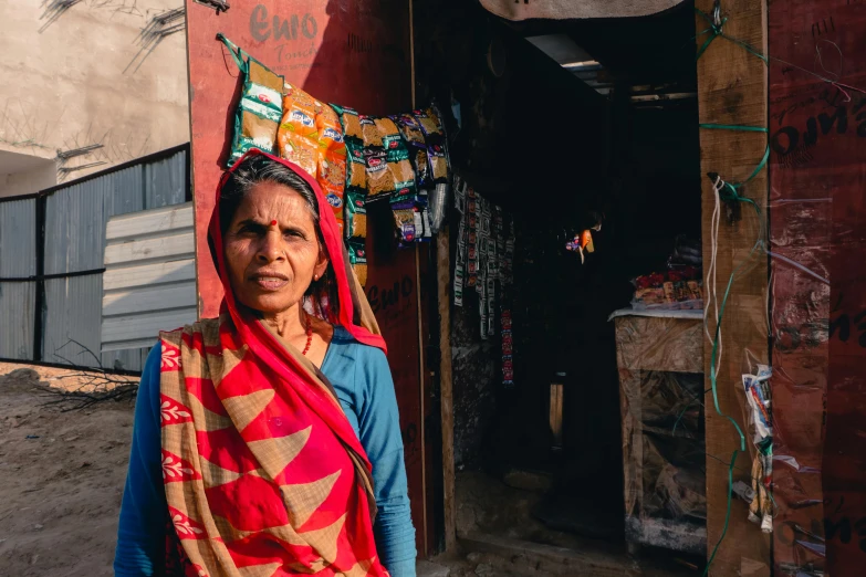 a woman standing in front of a red building, a portrait, pexels contest winner, on an indian street, stood outside a corner shop, thumbnail, crafts and souvenirs