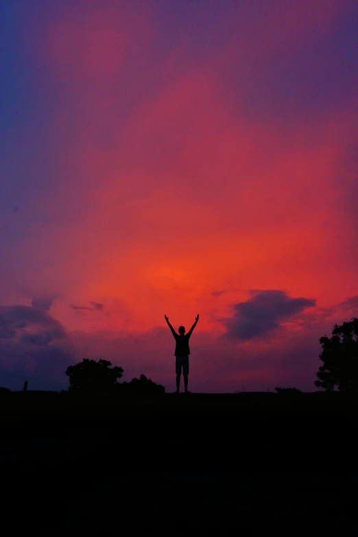 a person standing on top of a hill at sunset, red and purple, pose(arms up + happy), color photograph, siluettes