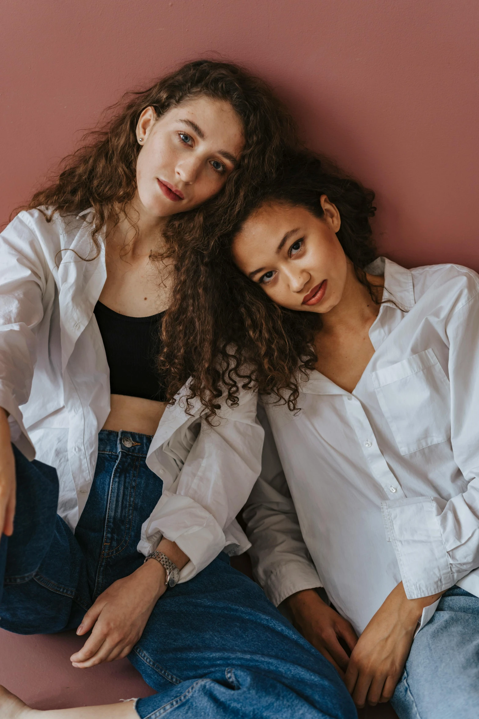 two women sitting next to each other on a pink surface, by Cosmo Alexander, trending on pexels, renaissance, wearing a white button up shirt, curls, portrait sophie mudd, outlive streetwear collection