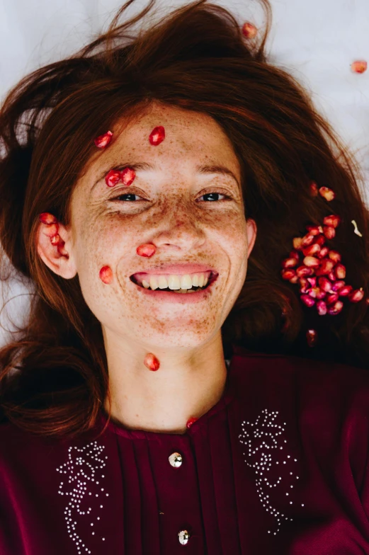 a woman laying on top of a bed covered in confetti, by Julia Pishtar, pomegranates, closeup on face, smiling into the camera, squashed berries