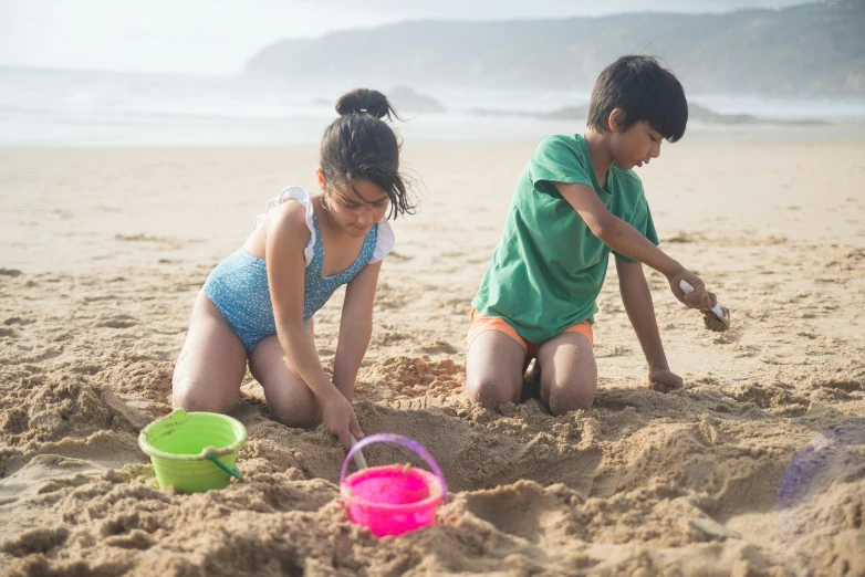 two children playing in the sand at the beach, by Arabella Rankin, pexels contest winner, nazare (portugal), mini model, thumbnail, male and female