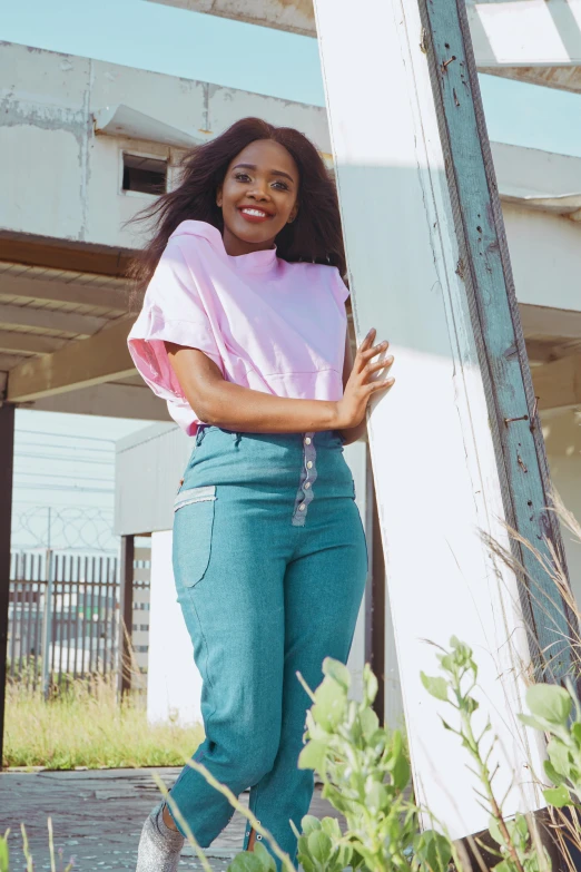 a woman posing for a picture in front of a building, pink and teal, wearing pants and a t-shirt, in style of nadine ijewere, curated collections