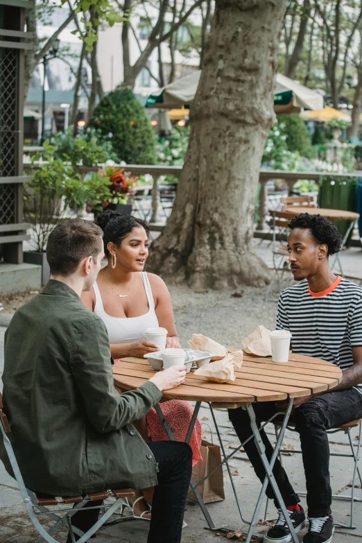 a group of people sitting around a wooden table, sitting on a park bench, in new york city, non-binary, cafe