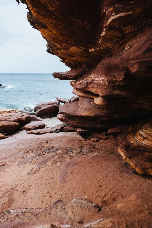 a couple of rocks sitting on top of a sandy beach, red sandstone natural sculptures, views to the ocean, watery caverns, up-close