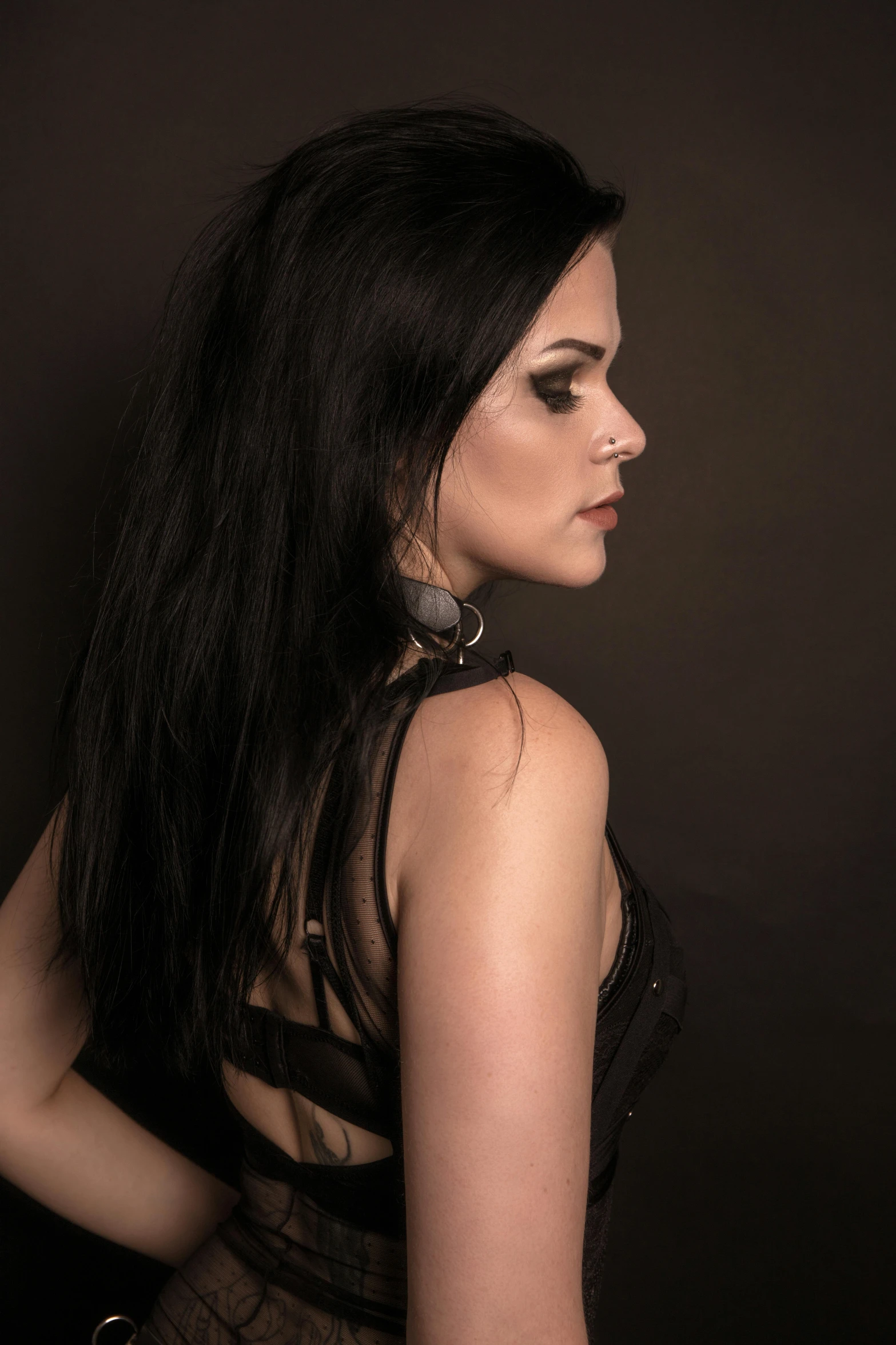 a woman in a black dress posing for a picture, an album cover, inspired by Claire Dalby, pexels contest winner, brown dark hair, black leather harness, profile view, close - up studio photo