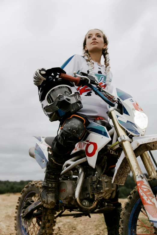 a woman sitting on a dirt bike in a field, off-white plated armor, race style, totally radical, close up details