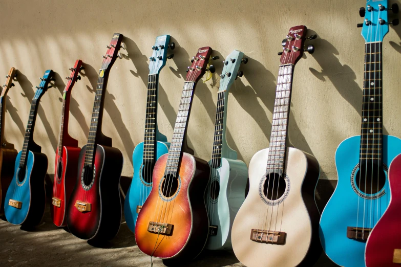 a row of guitars lined up against a wall, by Joe Bowler, shutterstock, ukulele, sunny sky, instagram post, coloured