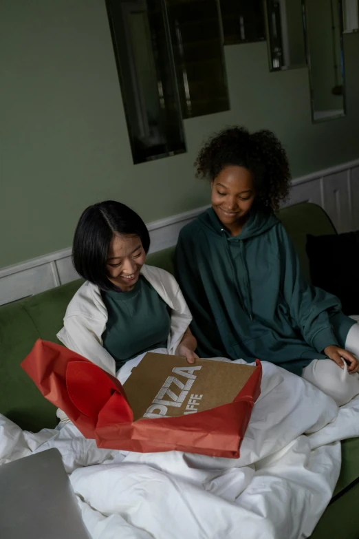 a couple of women sitting on top of a green couch, pizza box, tech robes, in a dark green polo shirt, kids playing