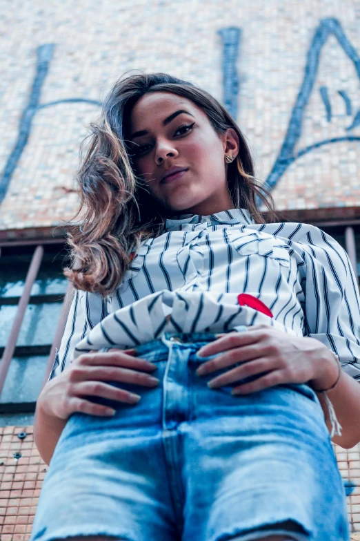 a woman standing in front of a graffiti covered building, by Niko Henrichon, trending on pexels, wearing stripe shirt, mila kunis, promotional image, top down view