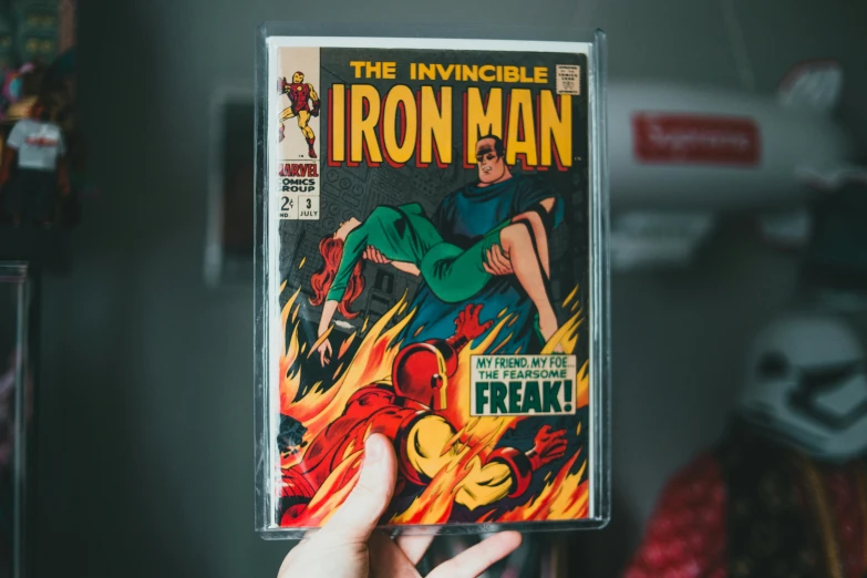 a person holding a comic book in their hand, an album cover, by Romain brook, pexels contest winner, iron man, jewel case, movie poster from 1960s, cassette