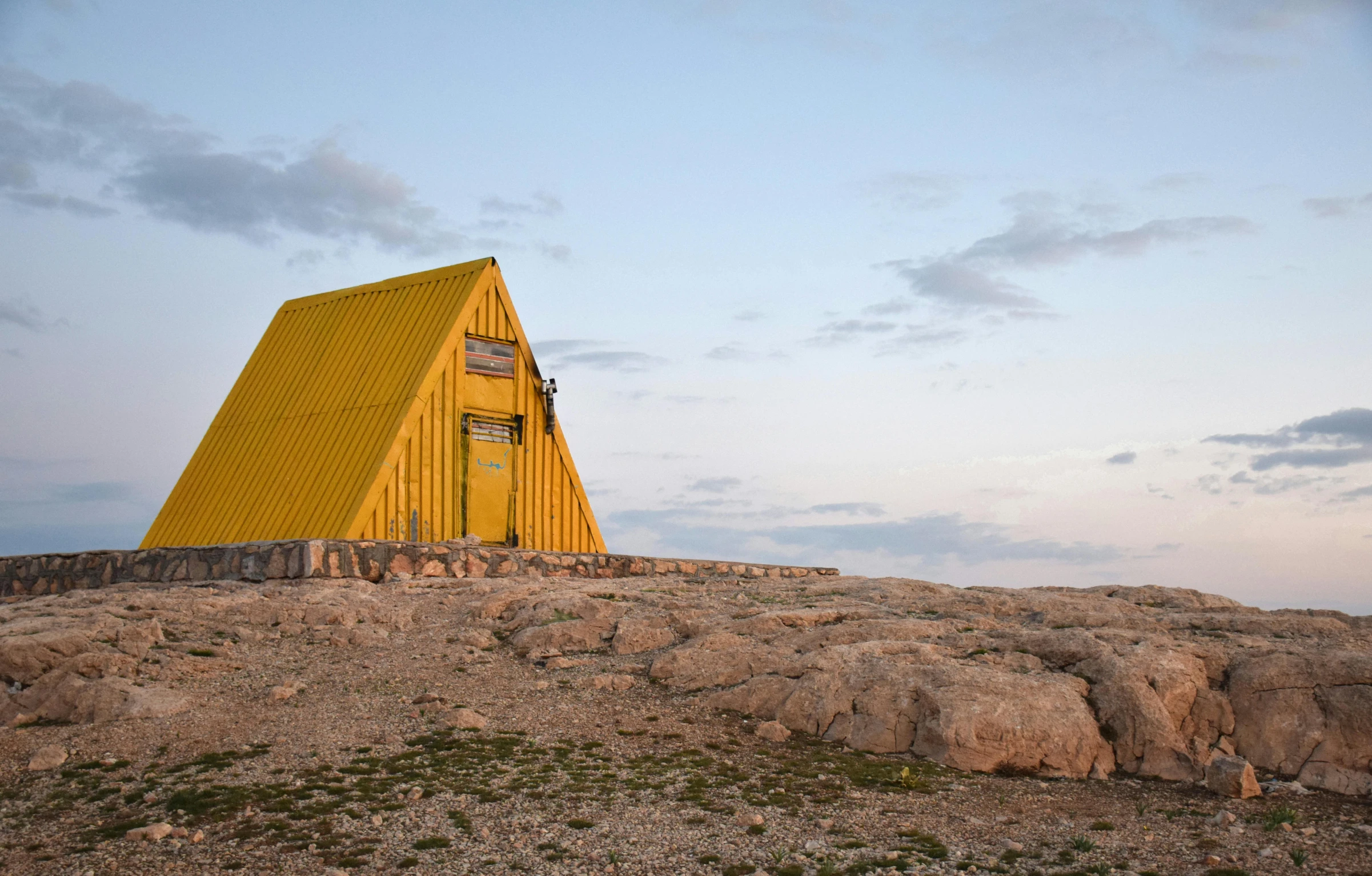 a yellow building sitting on top of a rocky hill, inspired by Wes Anderson, unsplash contest winner, hypermodernism, stood outside a wooden cabin, lada, trending on dezeen, archipelago