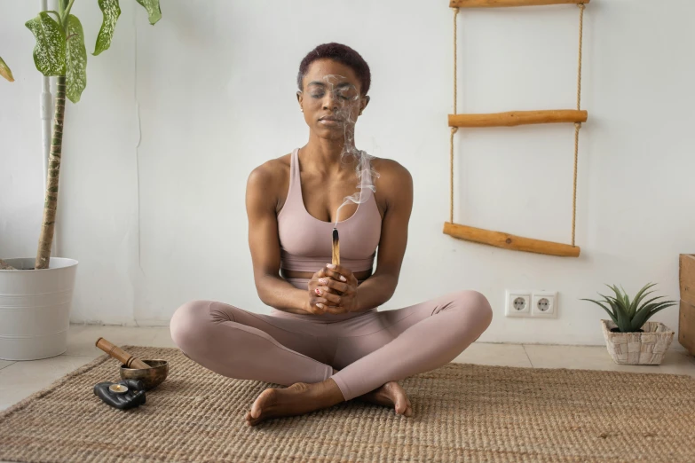 a woman sitting on the floor in a yoga pose, a portrait, pexels contest winner, figuration libre, glass and gold pipes, african woman, holding a wooden staff, low quality photo