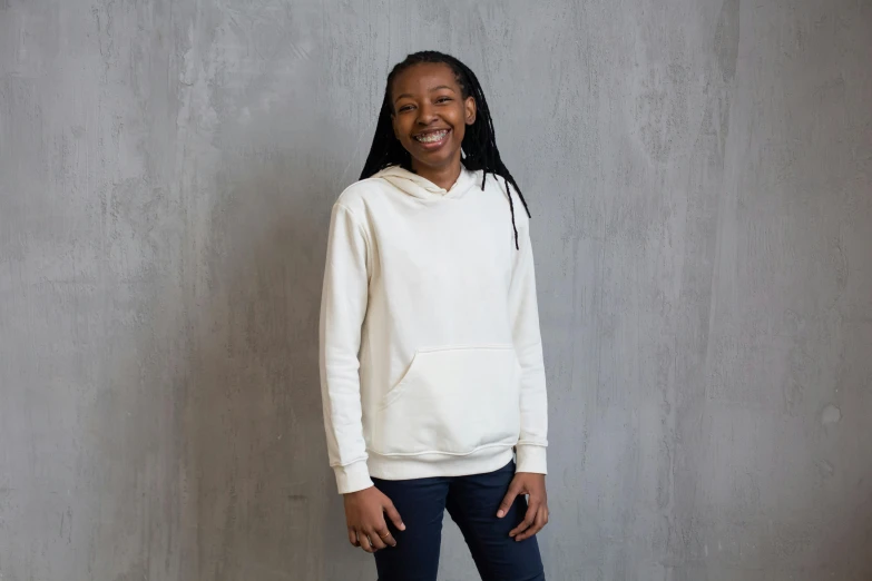 a woman standing in front of a wall wearing a white hoodie, inspired by Sarah Lucas, black teenage boy, neutral background, smiling girl, full product shot