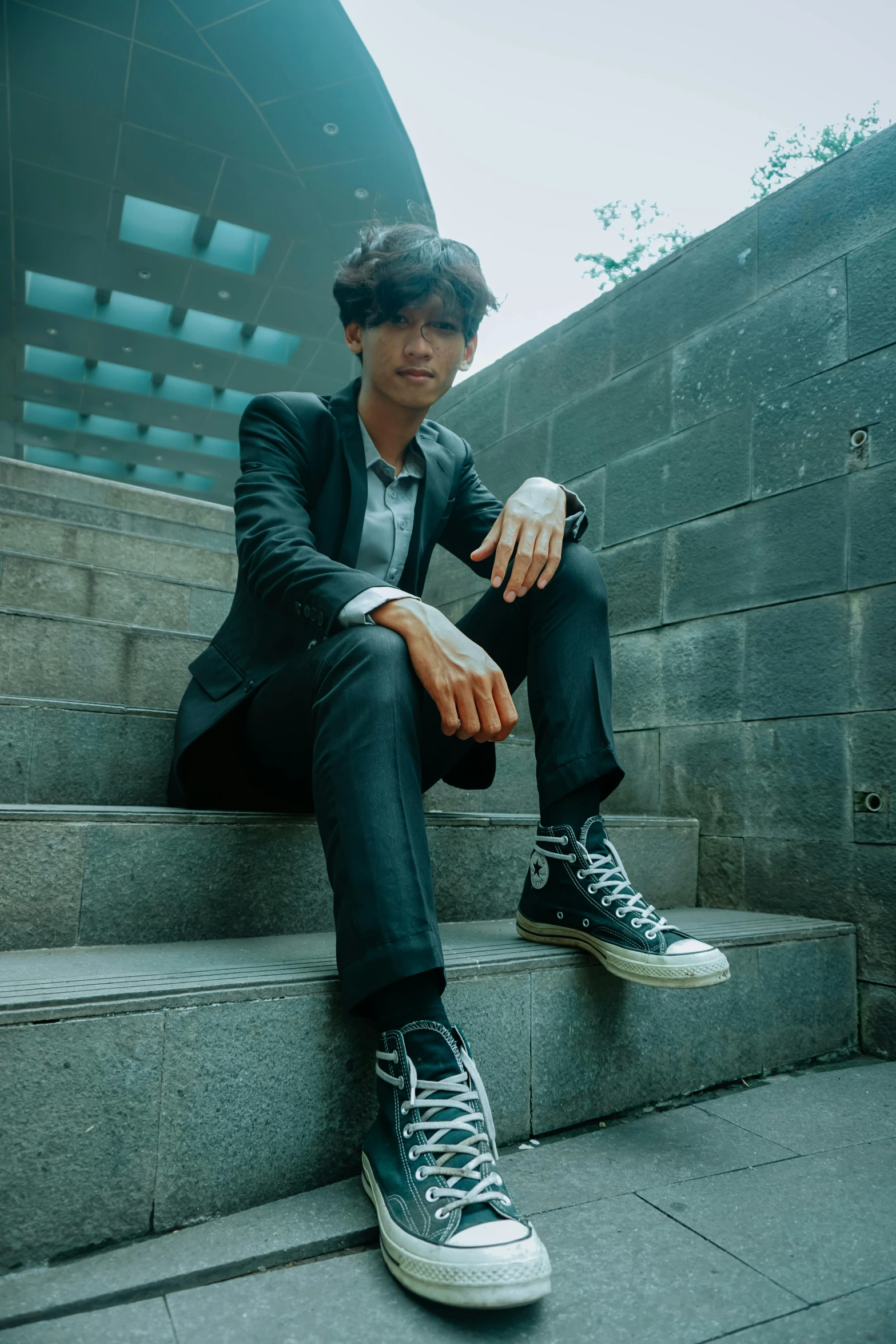 a man sitting on the steps of a building, an album cover, unsplash, androgynous person, wearing causal black suits, in style of lam manh, boyish