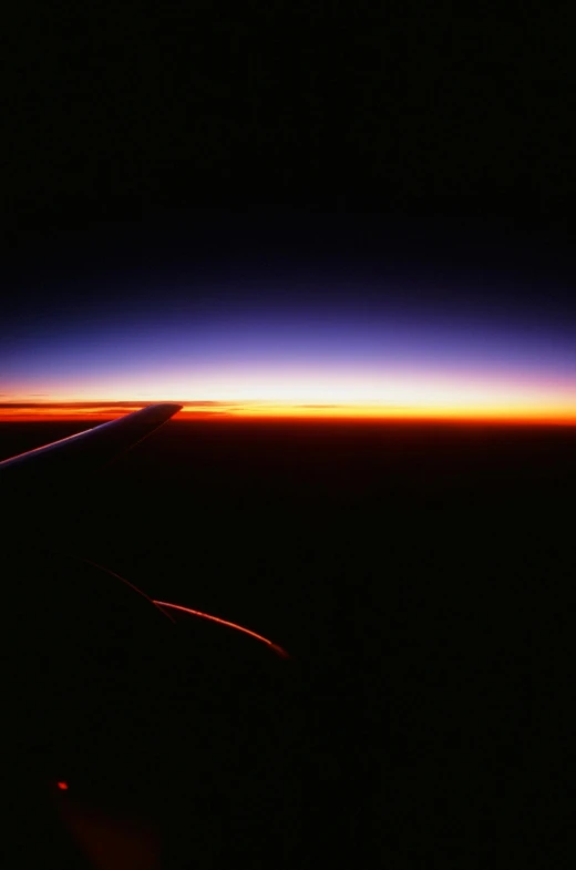 the wing of an airplane as the sun sets, by Peter Churcher, 1996, noctilucent, light red and deep blue mood, over the horizon