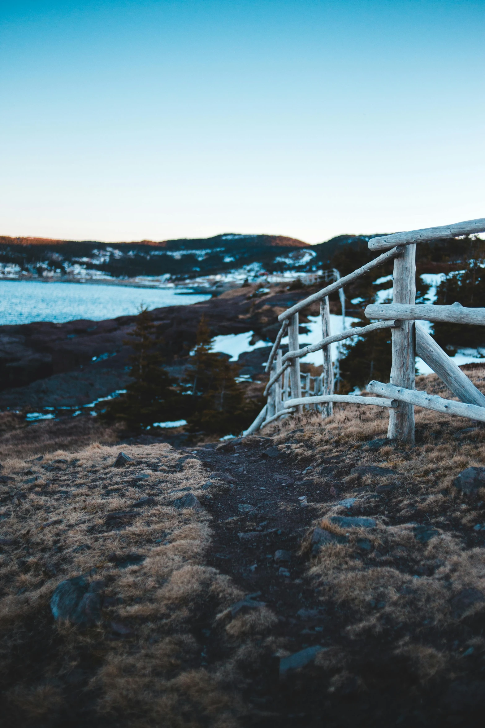 a wooden fence sitting on top of a hill next to a body of water, by Jesper Knudsen, unsplash, icey tundra background, low quality photo, pathway, views to the ocean