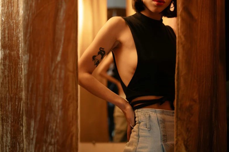 a woman standing in a doorway with a tattoo on her arm, trending on pexels, croptop, kiko mizuhara, cindy avelino, sleeveless