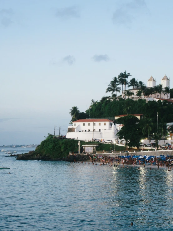 a group of people standing on top of a beach next to a body of water, salvador, swimming, palace on top of the hill, listing image
