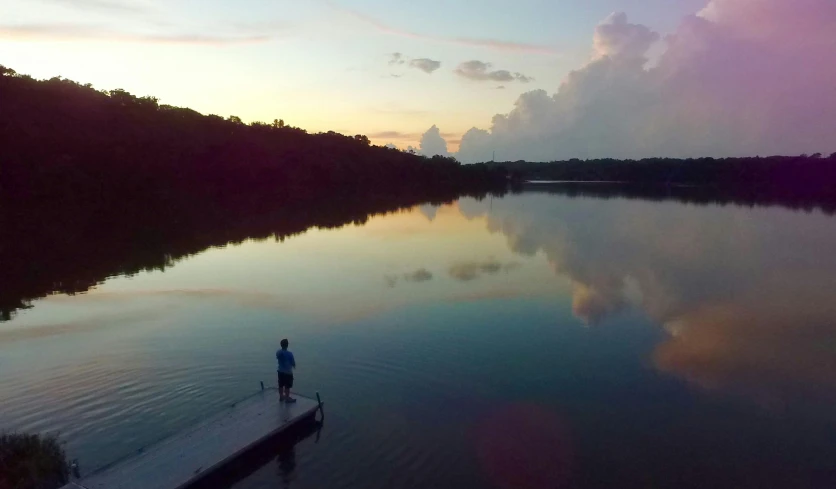 a person standing on a dock next to a body of water, at sunset, bird's eye view, backwater bayou, landscape photo
