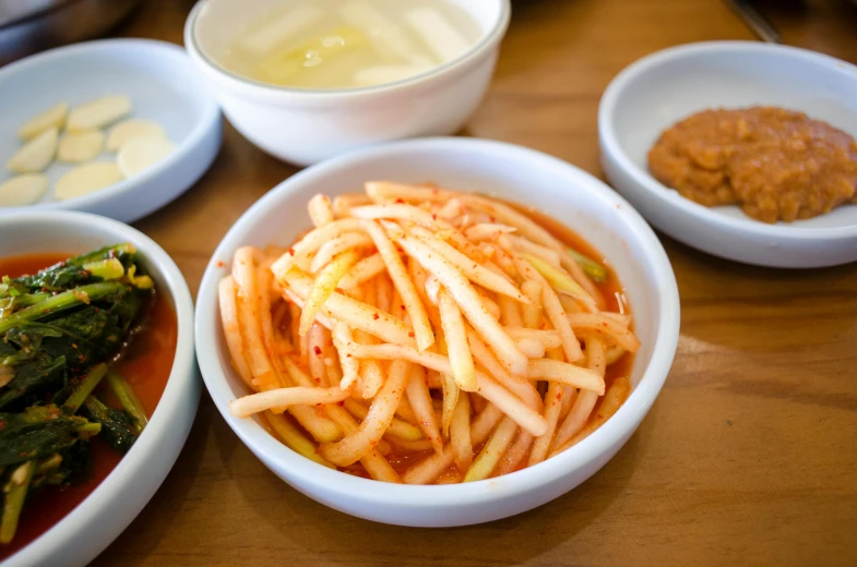 a wooden table topped with bowls of food, unsplash, squids, pickles, closeup photograph, square