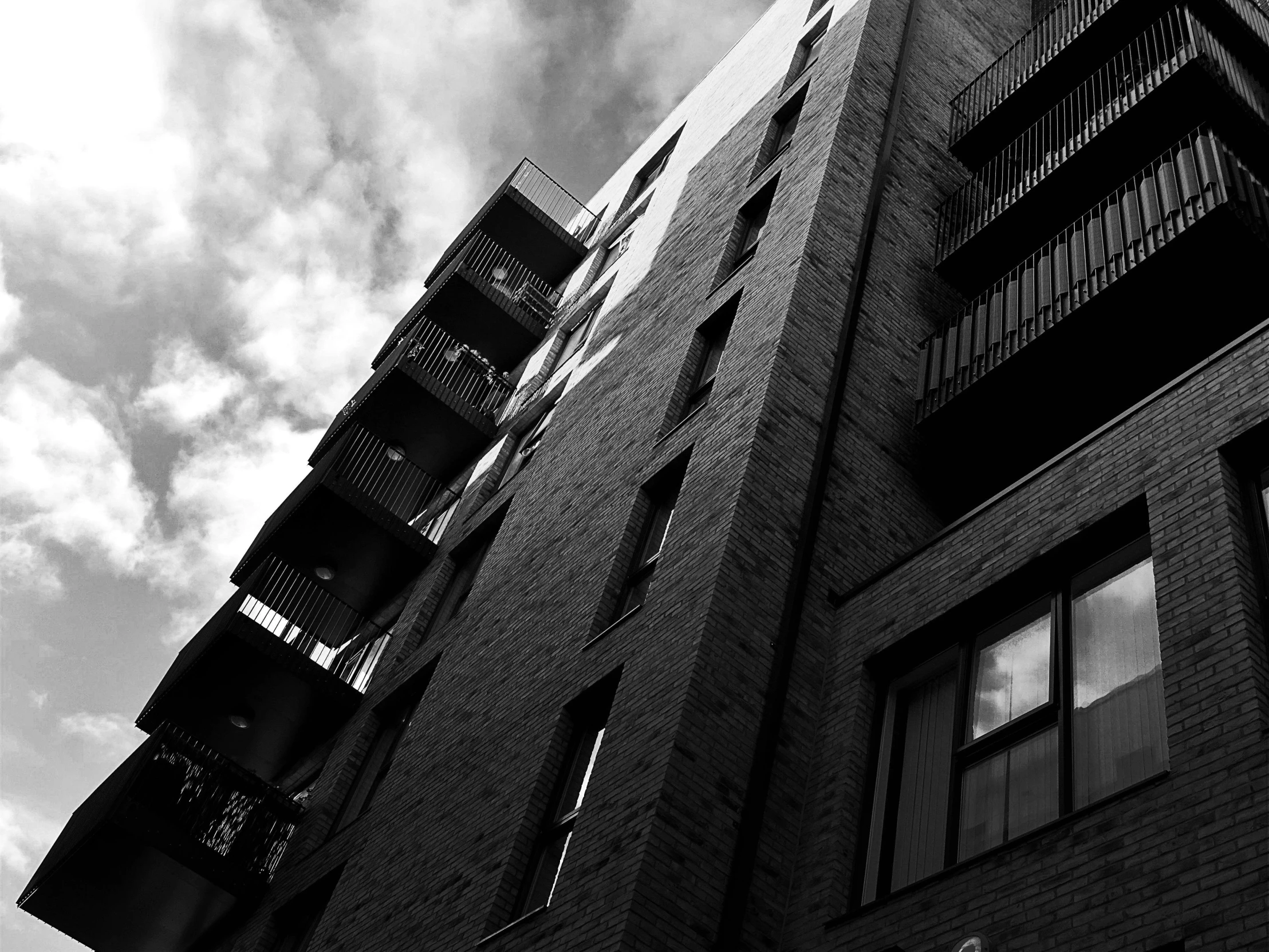 a black and white photo of a tall building, a black and white photo, unsplash, brick building, balconies, moody sky at the back, ten flats