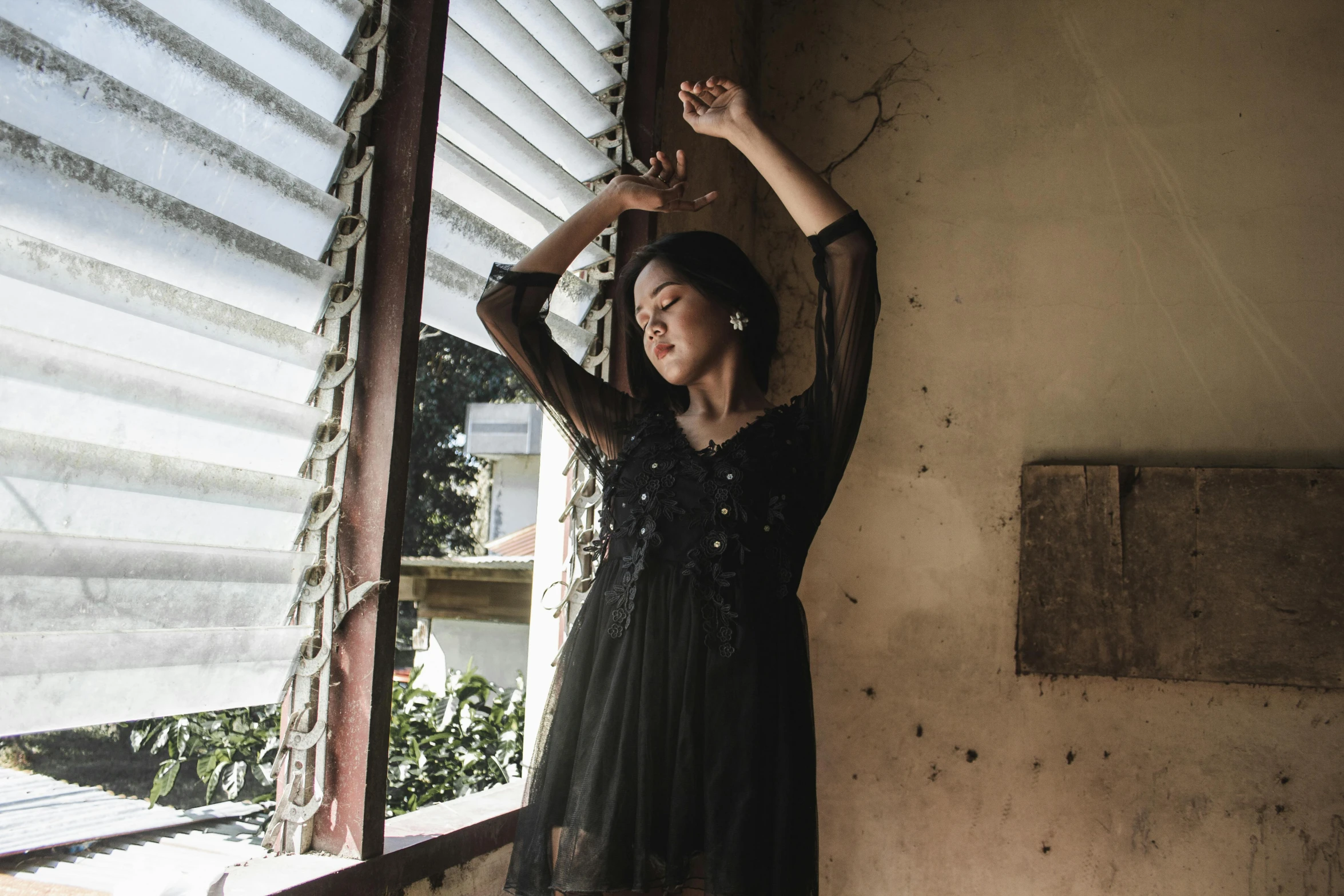 a woman in a black dress standing in front of a window, inspired by Elsa Bleda, pexels contest winner, arabesque, young asian girl, frantic dancing pose, an abandoned, satisfied pose