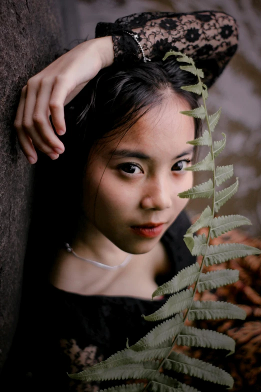 a woman in a black dress leaning against a wall, inspired by Tang Yifen, pexels contest winner, realism, leaf hair, detailed face of a asian girl, on a branch, ((portrait))