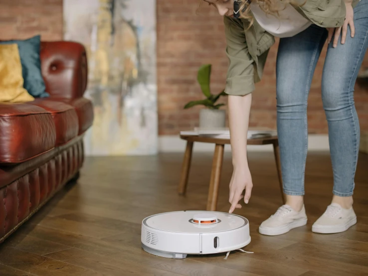 a woman standing next to a robot on a wooden floor, detailed product image, vacuum, white and orange, round robot
