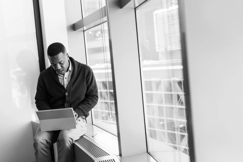 a man sitting on a window sill using a laptop, a black and white photo, rj palmer, jordan lamarre - wan, promo image, people at work