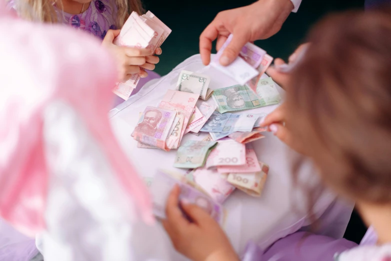 a group of people sitting around a table with money, by Emma Andijewska, pexels contest winner, hurufiyya, pink, children's, modest, thumbnail