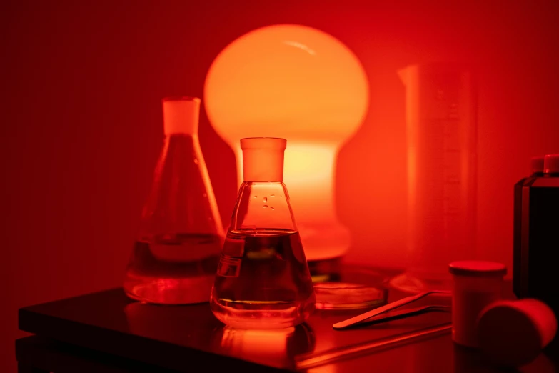 a lamp that is on top of a table, a still life, pexels, synthetism, beakers of colored liquid, with red haze, indoor lab scene, orange glow