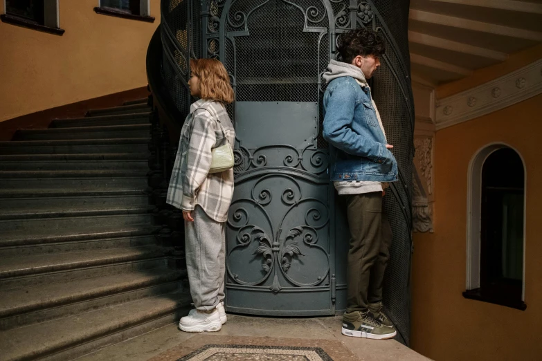 a man and a woman standing in front of a door, by Matija Jama, pexels contest winner, art nouveau, baggy jeans, teenage boy, 1 staircase, shy looking down