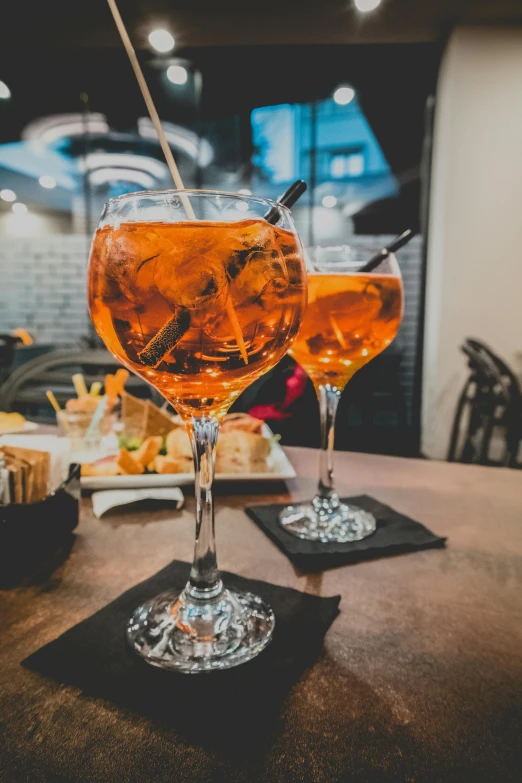 a couple of wine glasses sitting on top of a wooden table, by Carlo Martini, pexels, renaissance, orange and black, chianti molotov cocktails, square, served with pasta