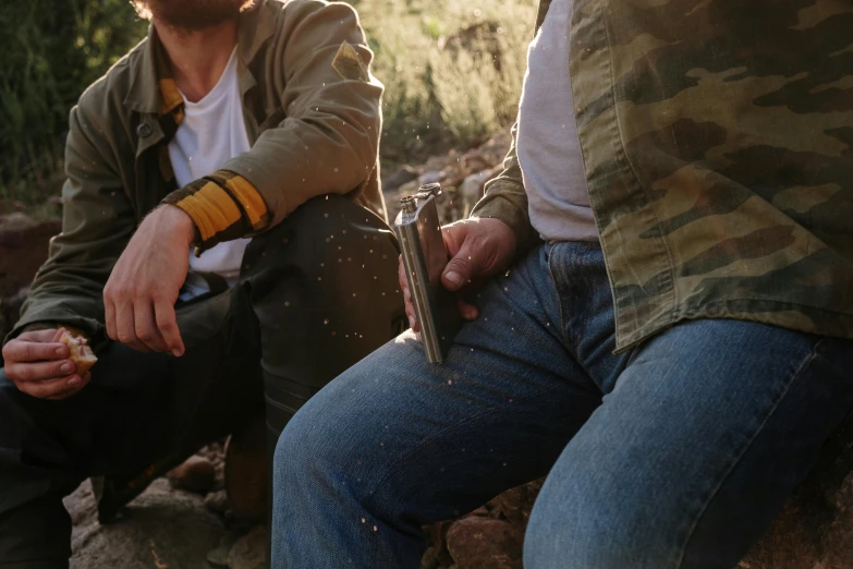 a couple of men sitting next to each other, trending on pexels, gun scraps, in the australian outback, holding a torch, background image