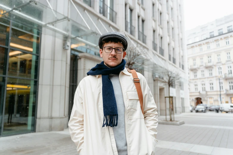 a man standing on a sidewalk in front of a building, by Nina Hamnett, pexels contest winner, bauhaus, wearing a french beret, avatar image, jewish young man with glasses, wearing a white winter coat