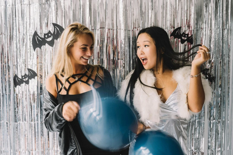 a couple of women standing next to each other holding blue balloons, a photo, trending on pexels, beistle halloween decor, black and silver, closed limbo room, college girls