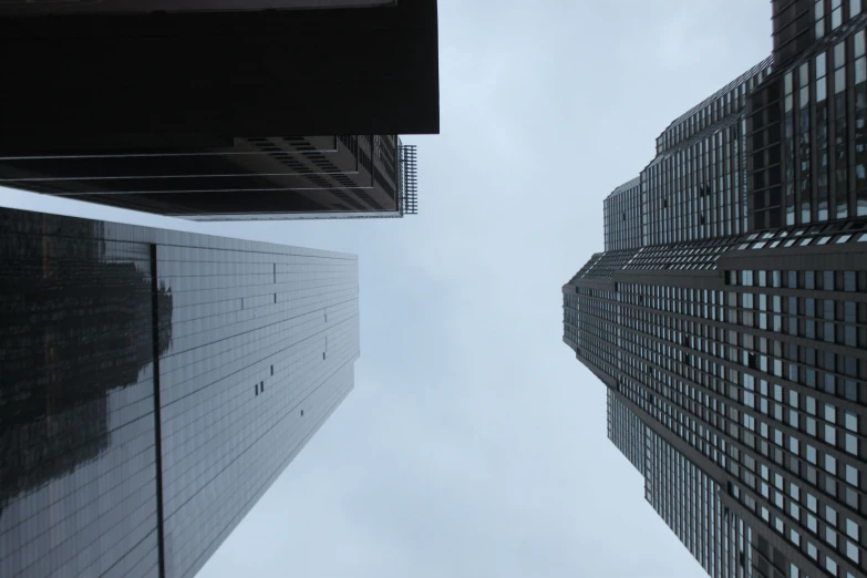 a couple of tall buildings next to each other, inspired by Thomas Struth, pexels contest winner, postminimalism, big overcast, worm\'s eye view, low quality photo, gray skies